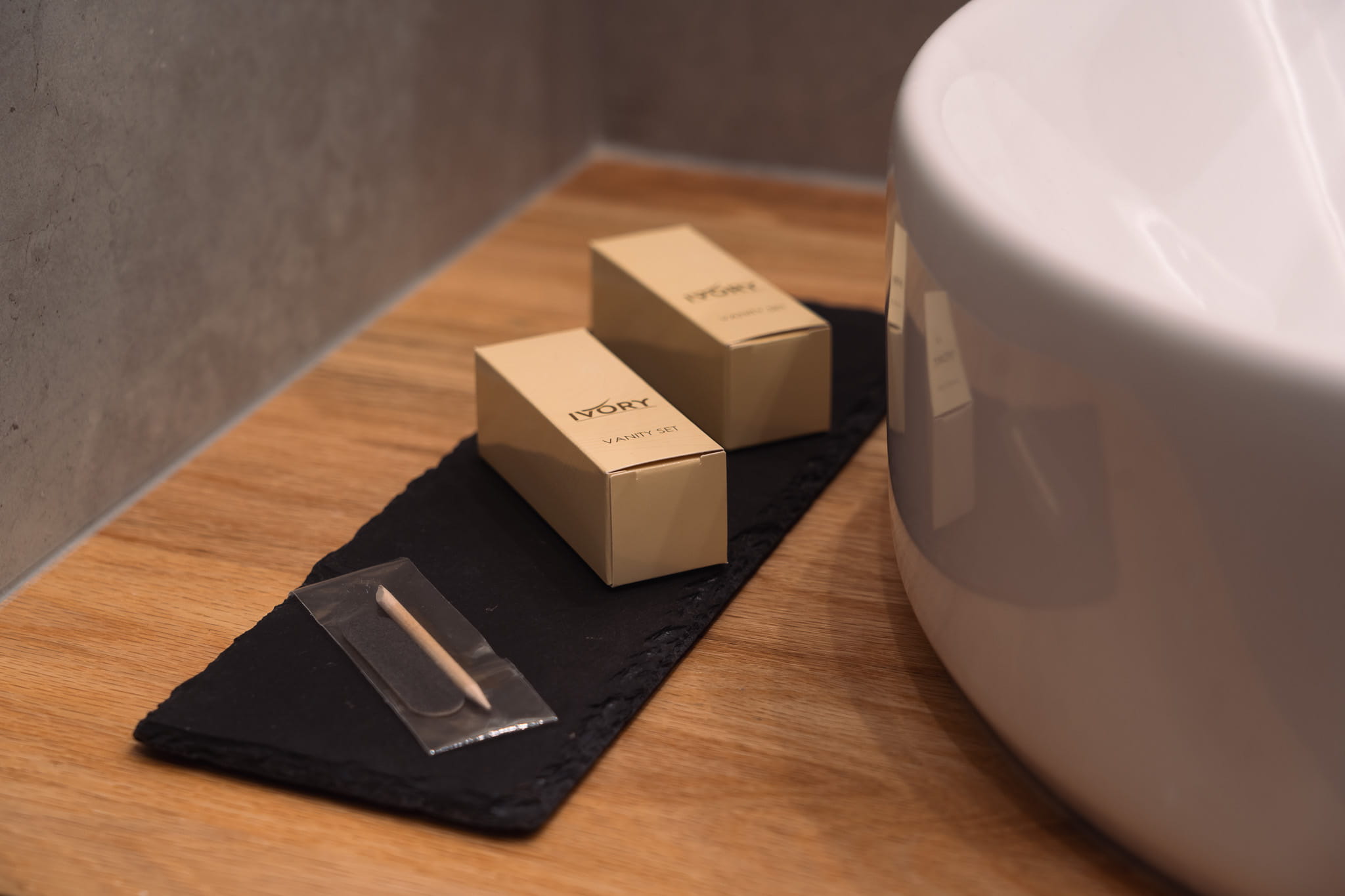 Vanity set boxes on a black tray next to a white sink on a wooden countertop.