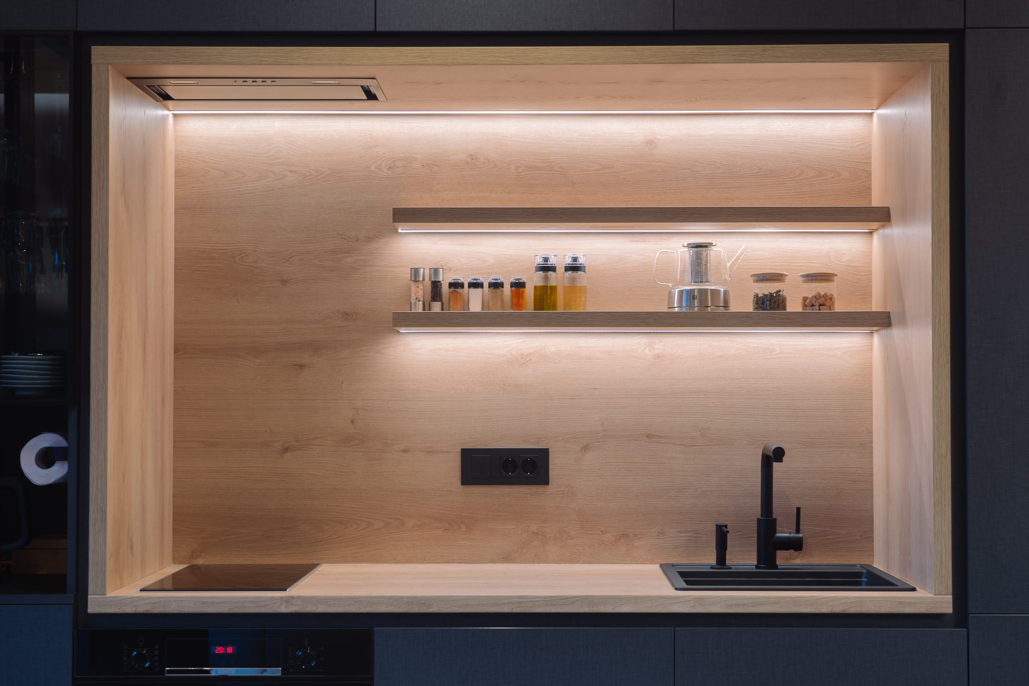 Modern kitchen nook with wooden shelves holding spices and containers, black sink, and induction cooktop.