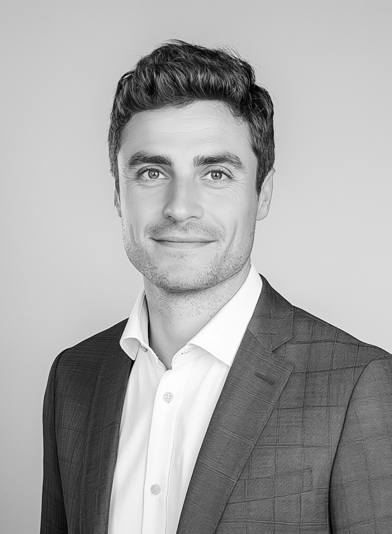 Smiling man with short hair wearing a checkered suit jacket and white shirt, against a plain background.