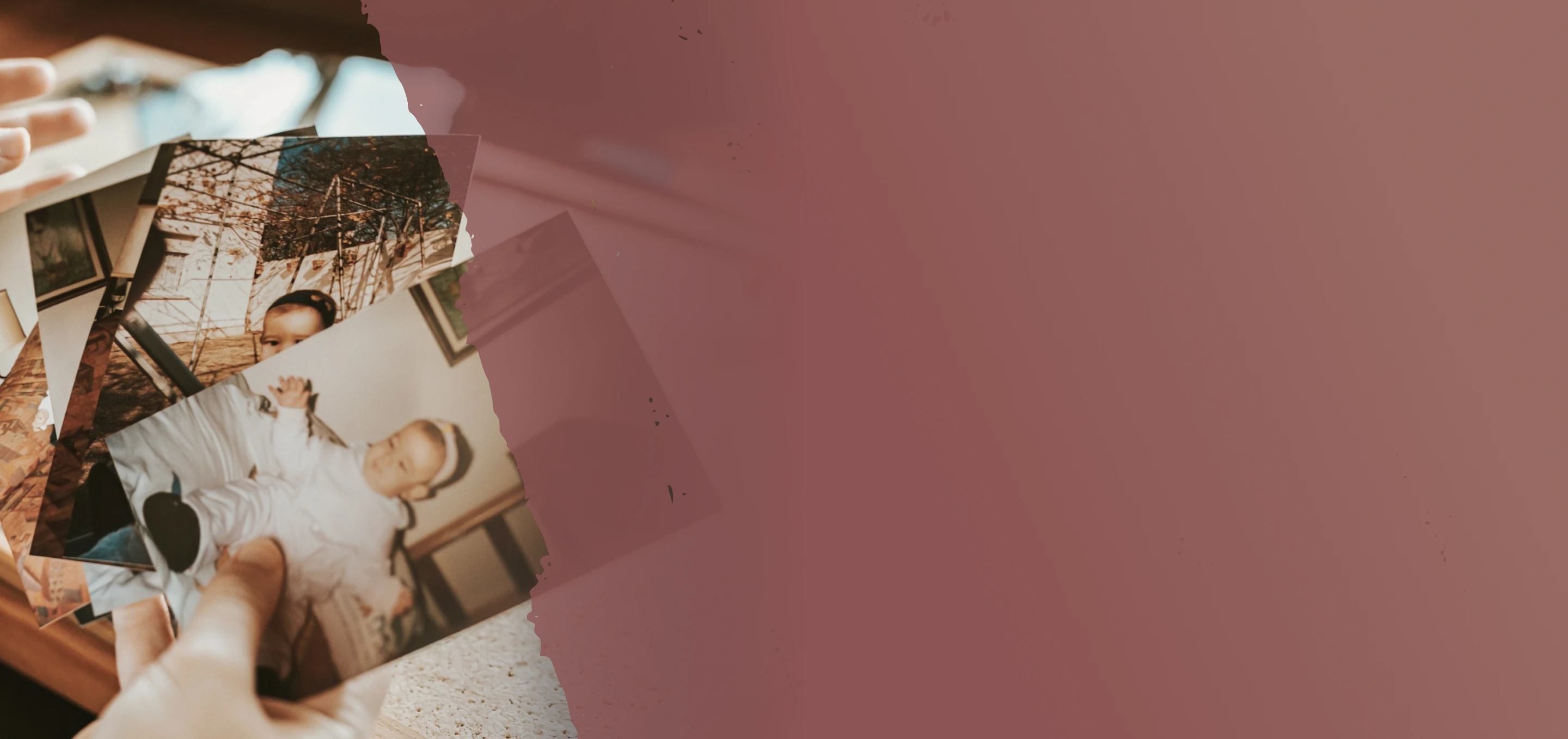 Hand holding a stack of old printed photos, including one of a baby dressed in white.