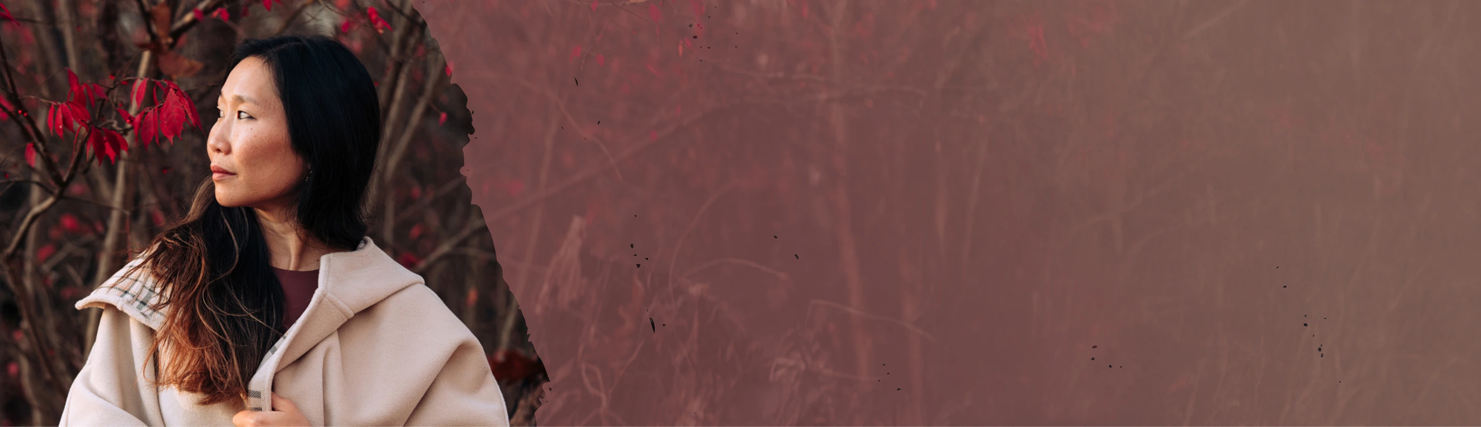 Founder Rachel Forbes wearing a light beige coat standing outdoors near red-leaved branches, looking to the left.