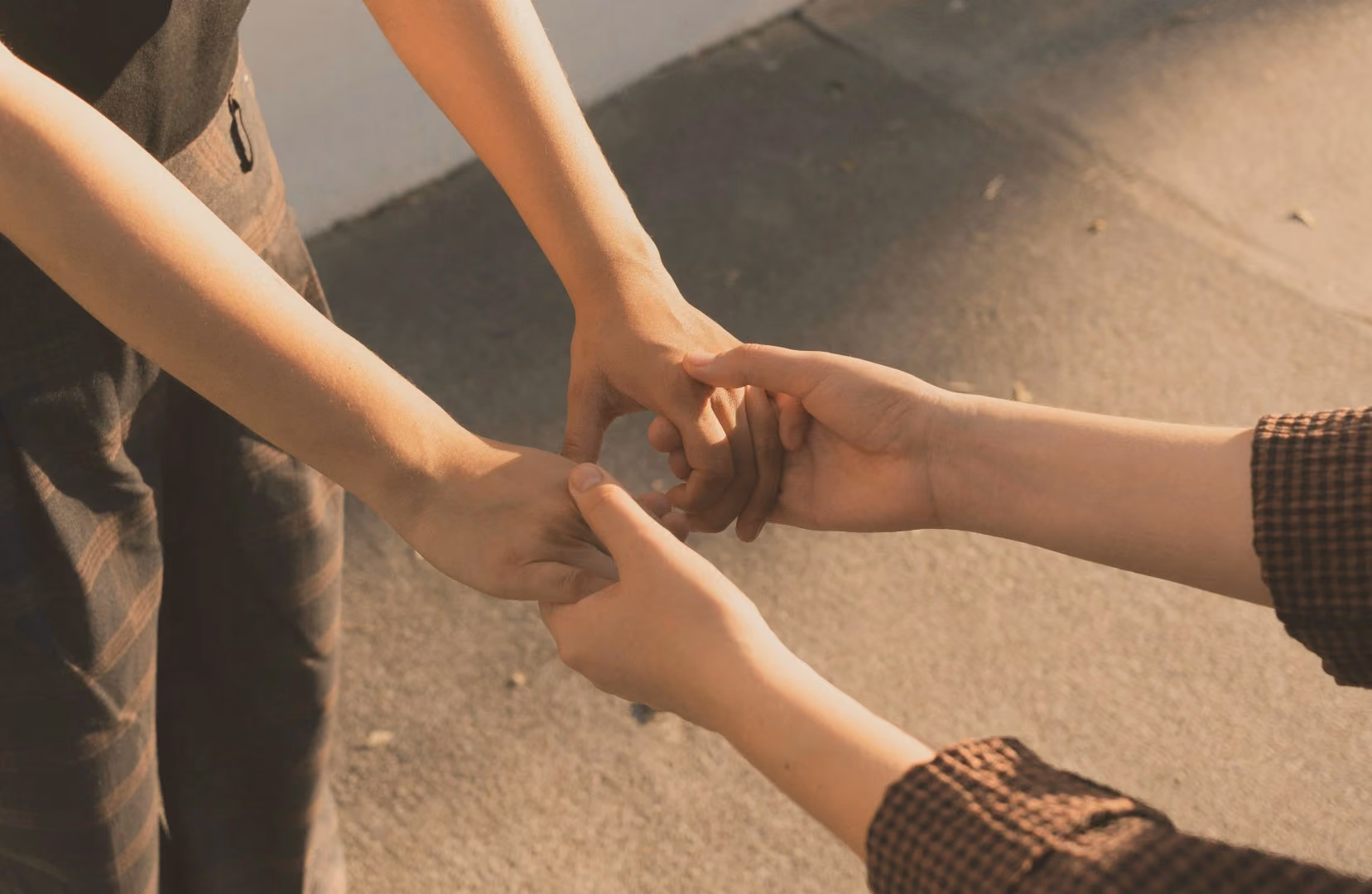 Two people holding hands gently outdoors on a sunlit pavement.