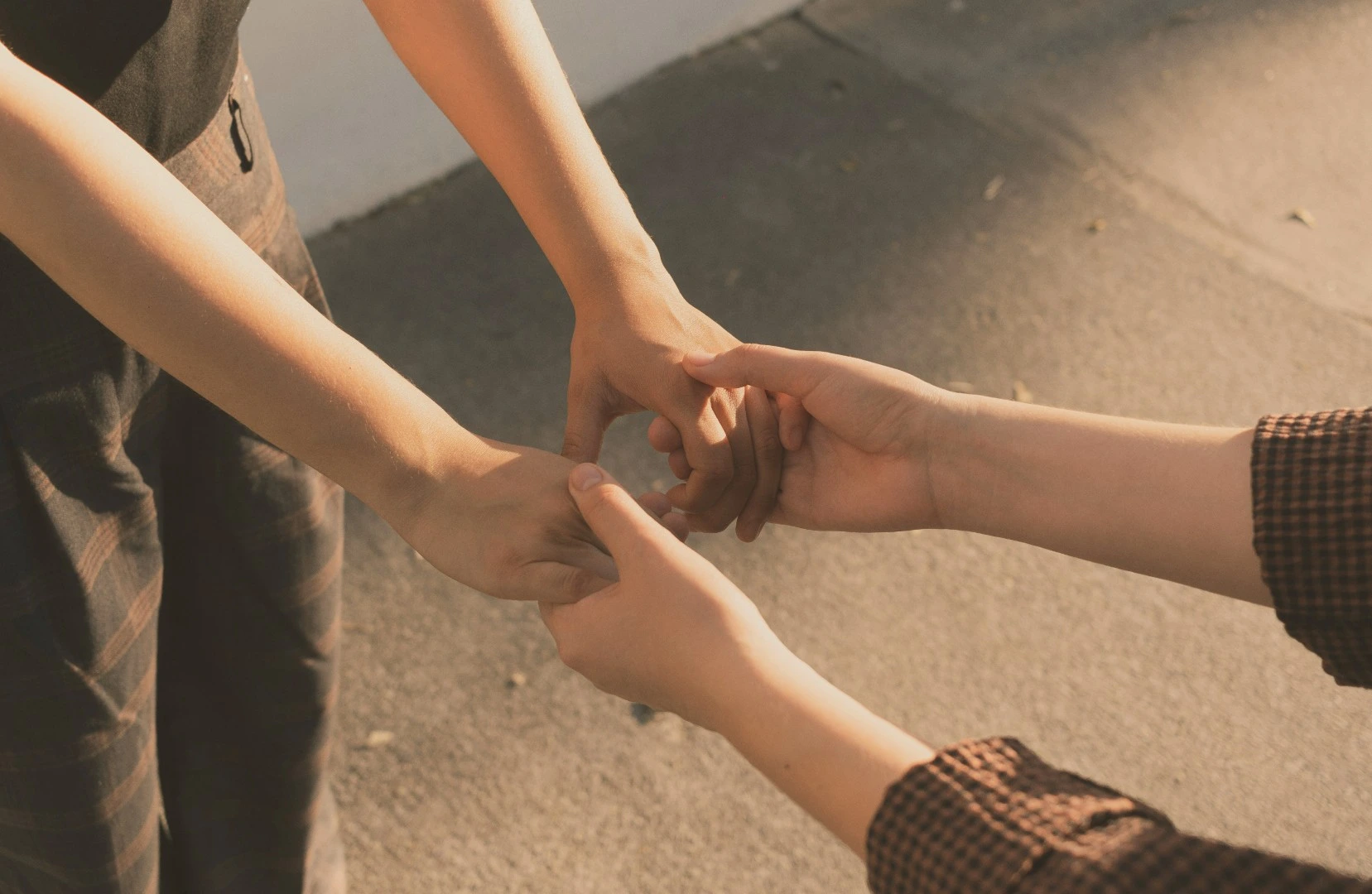 Two people holding hands gently outdoors on a sunlit pavement.