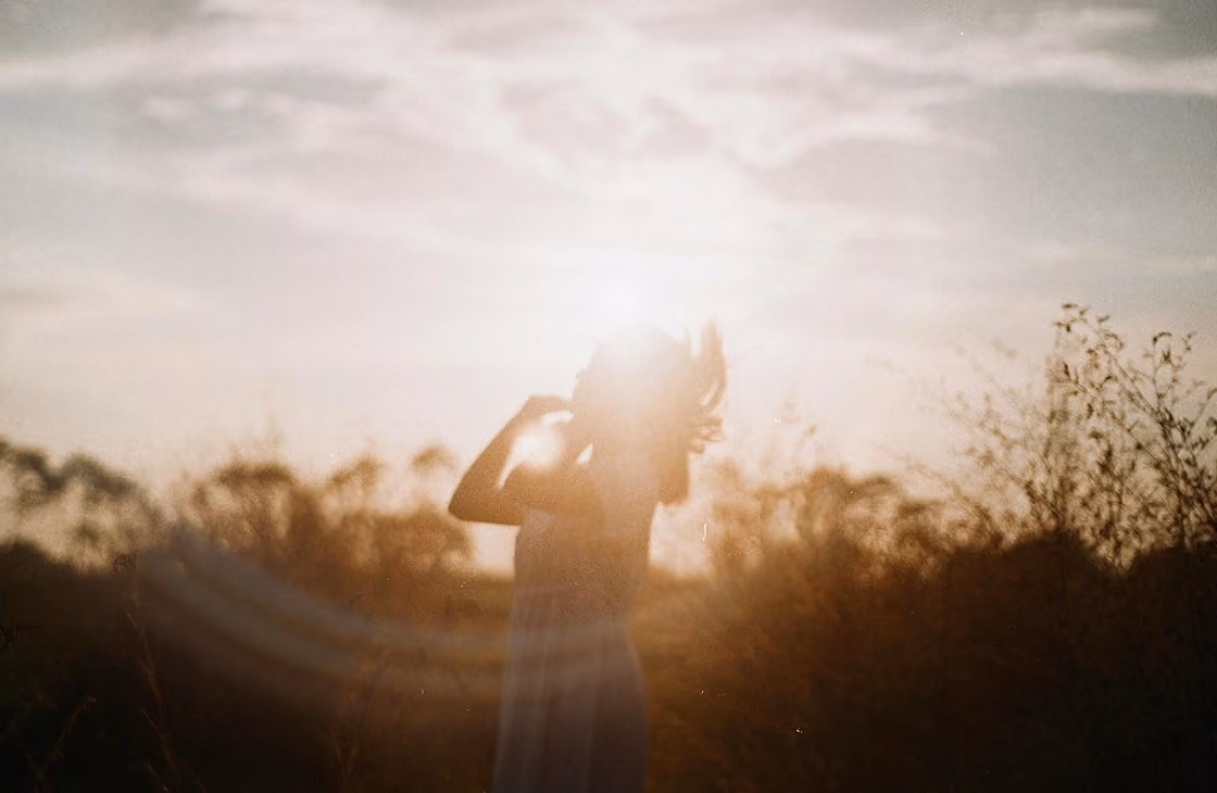 Silhouette of a person standing in a field with sunlight behind them during sunset.