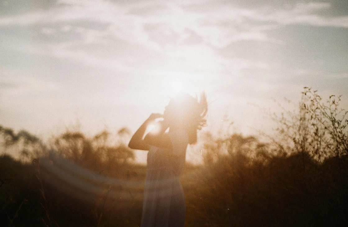 Silhouette of a person standing in a field with sunlight behind them during sunset.