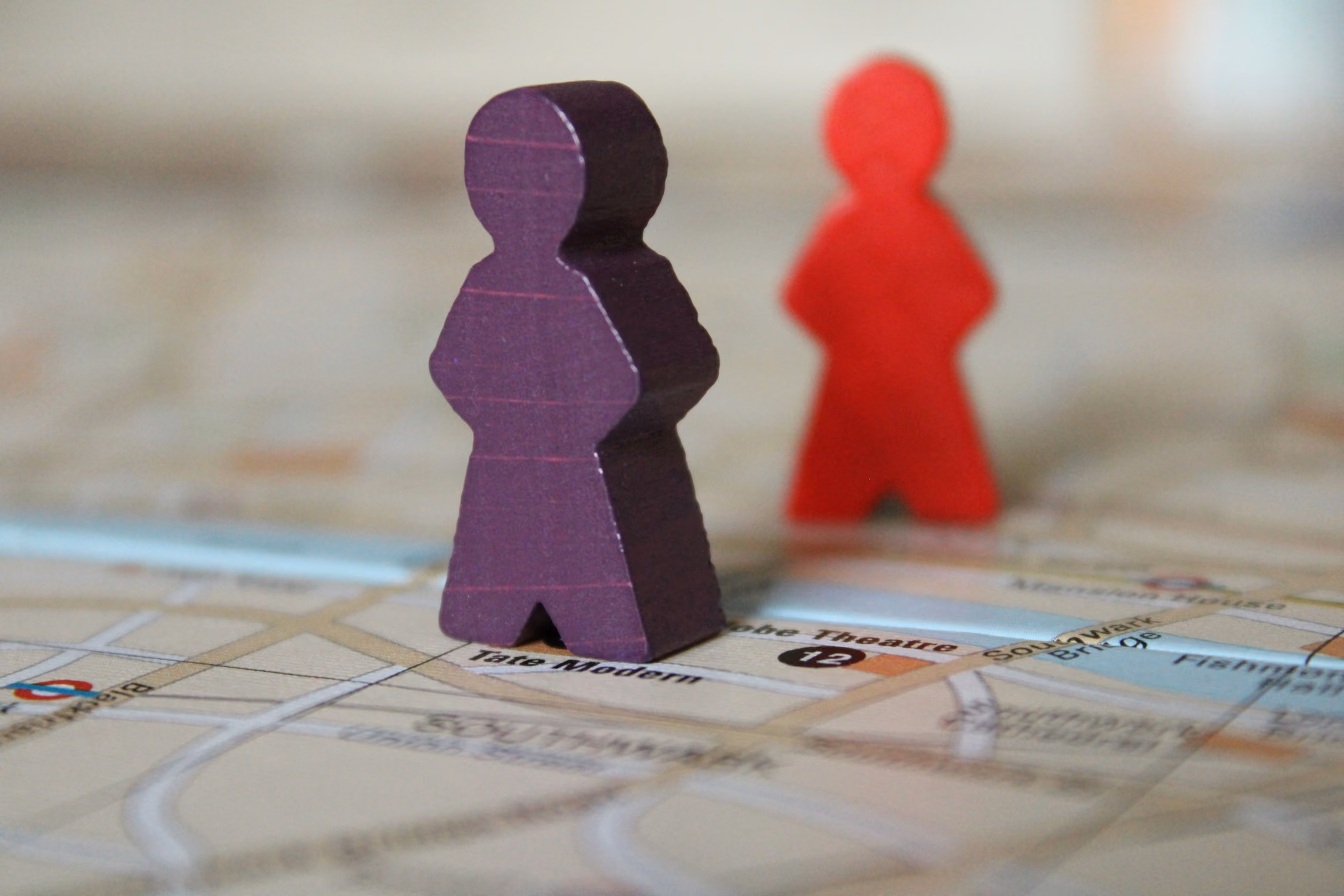 Two game style people markers on a city map, with a purple figure in sharp focus in the foreground and a red figure blurred in the background.