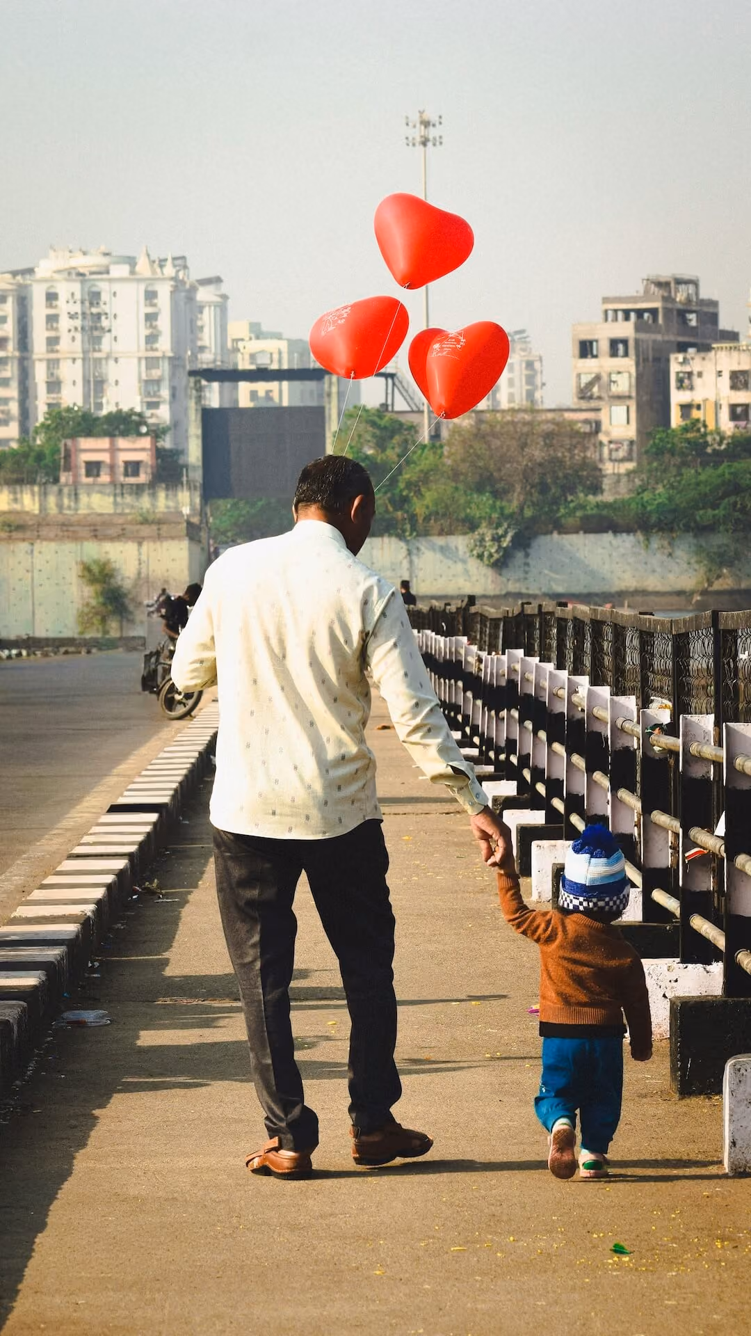 Adult and child holding hands while walking with red heart balloons, representing attachment based therapy and healthier relationships.