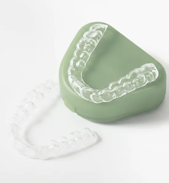 Clear dental aligners displayed against a white background, with one placed on a green holder and the other lying beside it.