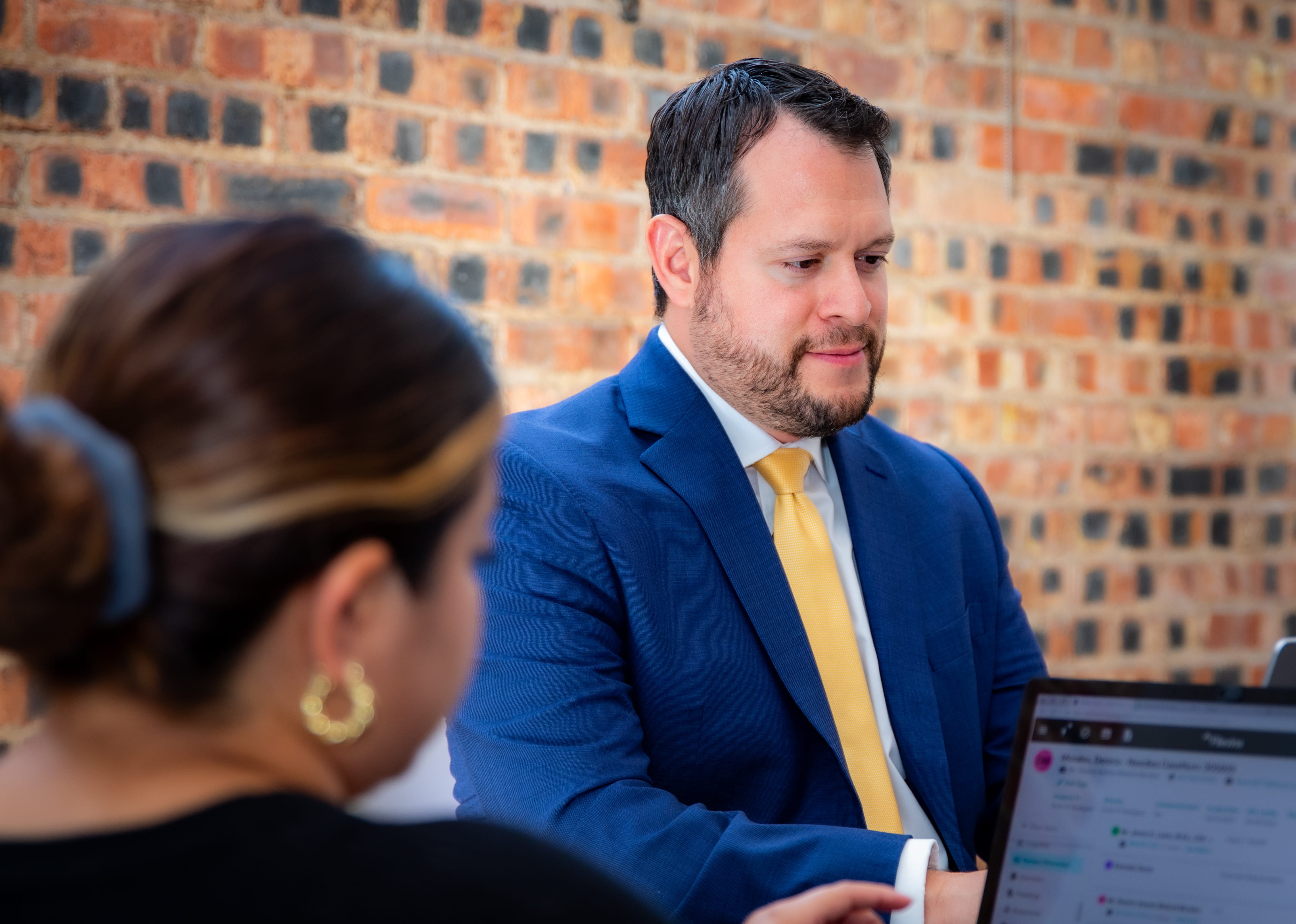 A diverse business team meeting in a modern conference room, collaborating around a table with laptops. The team members are engaged in a discussion while reviewing information on their screens.