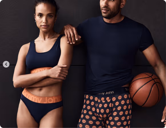 Man and woman posing against a black wall in Tommy John clothes.