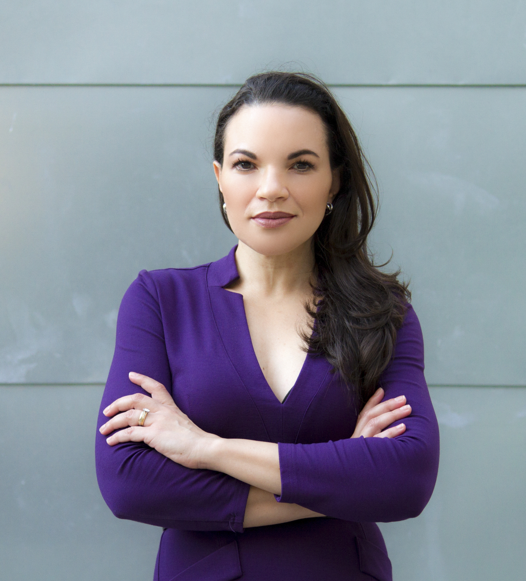 Confident woman with crossed arms wearing a purple dress against a gray background.