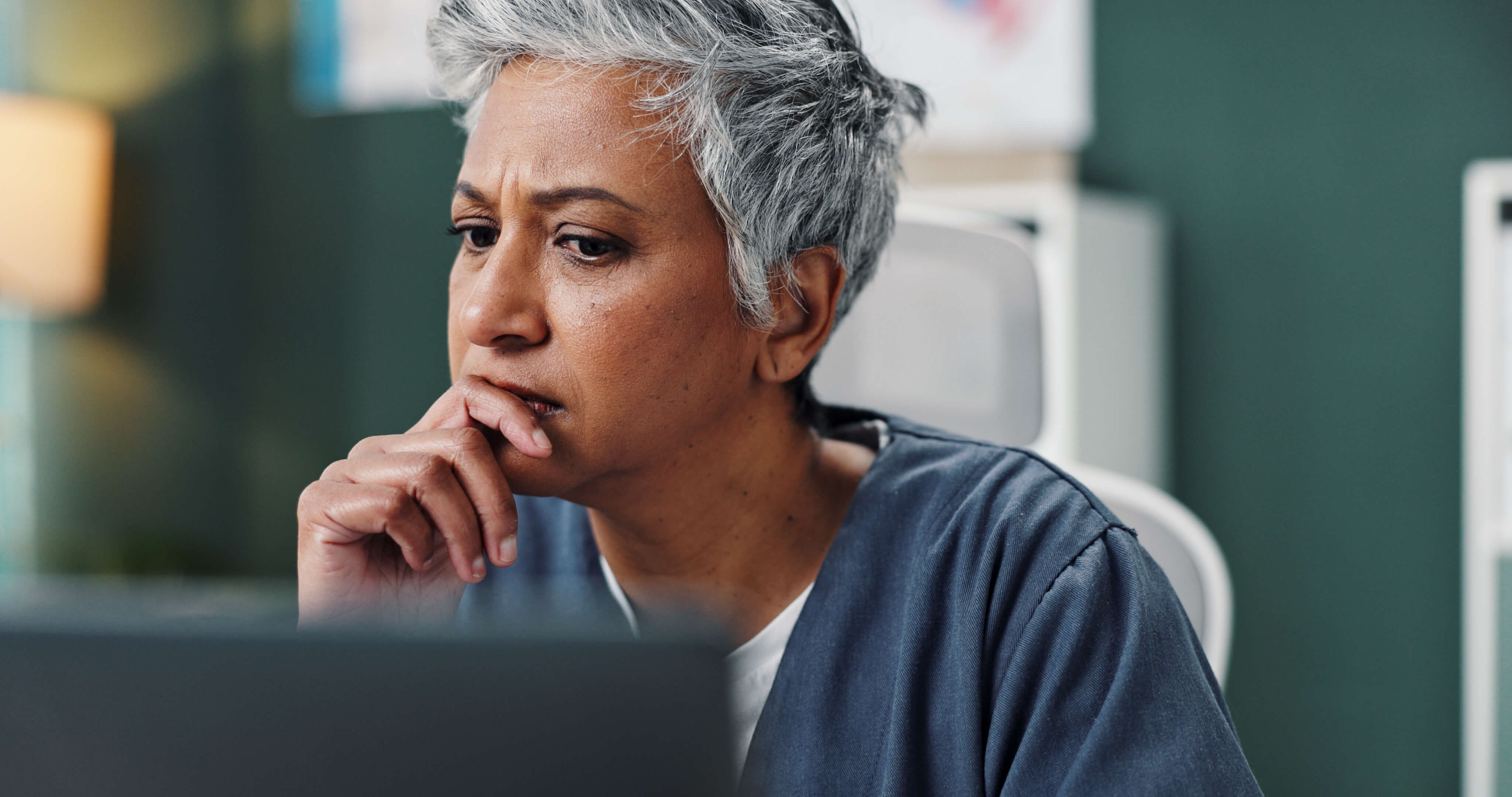 Worried woman with short gray hair looking at a computer screen, resting her hand near her mouth.