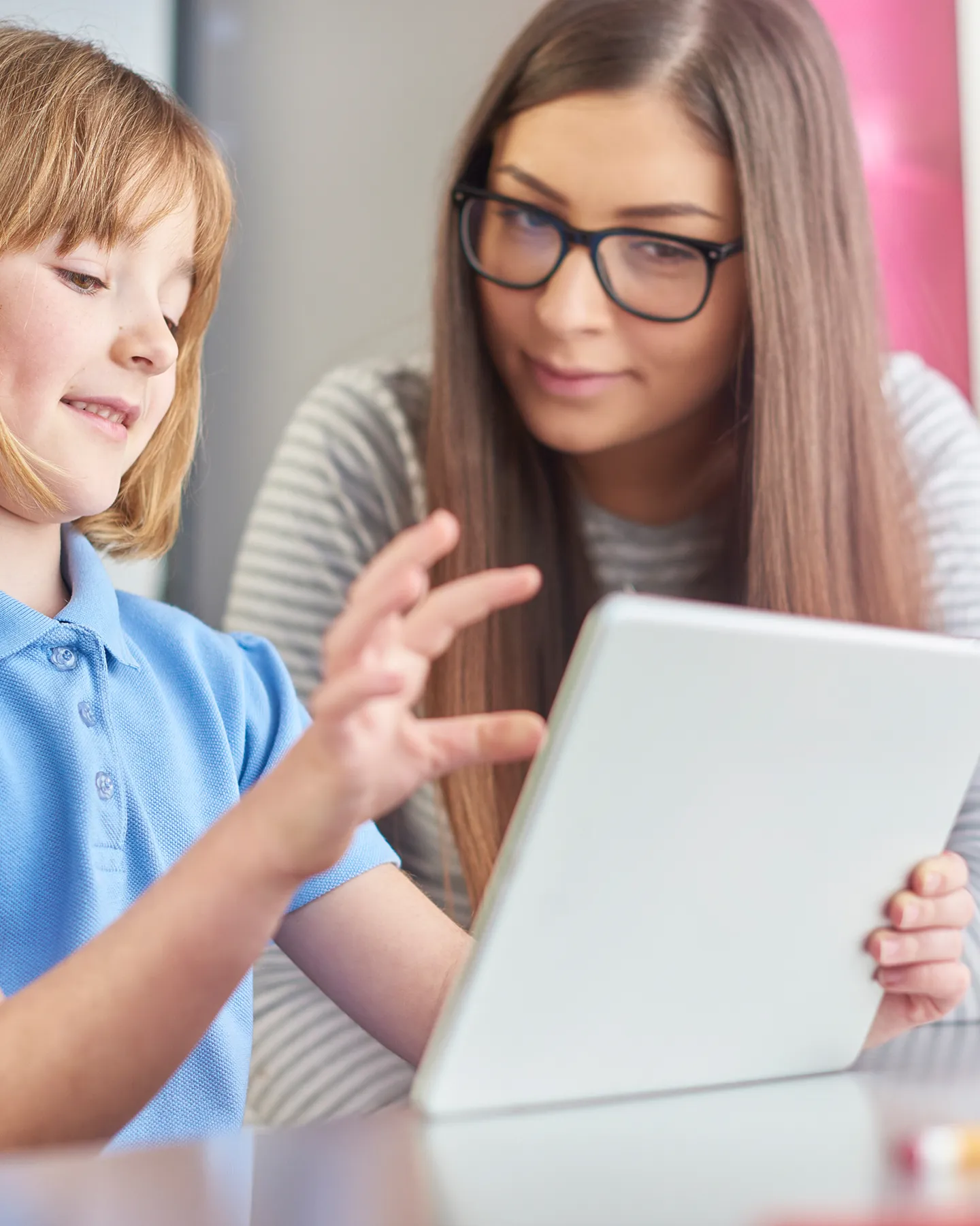 Teacher helps child use tablet computer in classroom