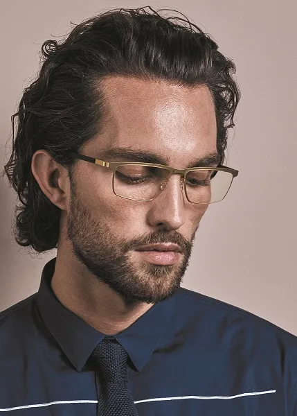 Stylish man with curly hair and glasses looking down in blue shirt