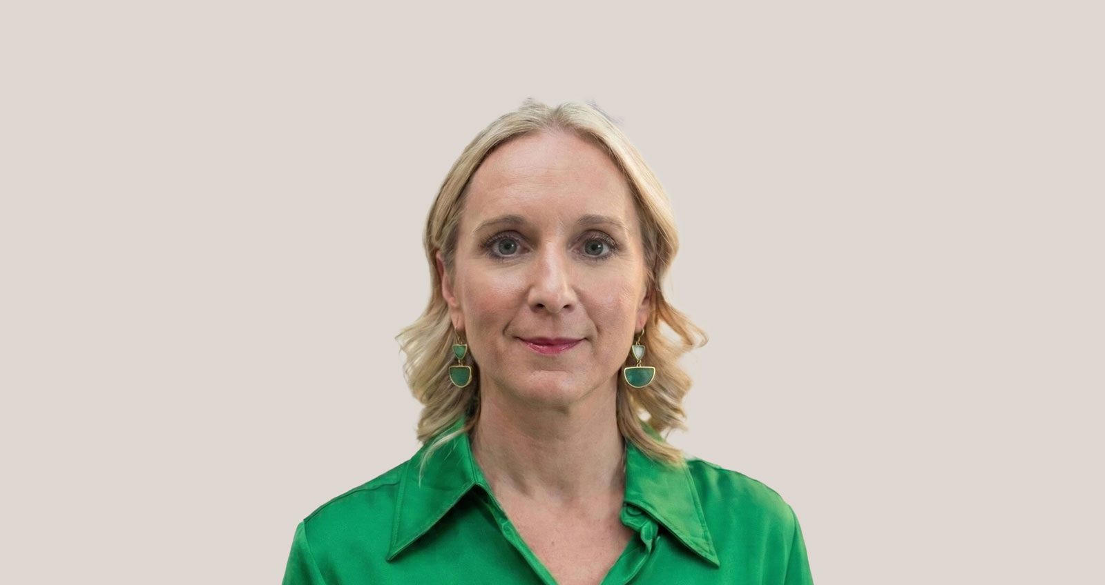 Mujer rubia con cabello corto y rizado lleva una blusa verde y pendientes verdes.
