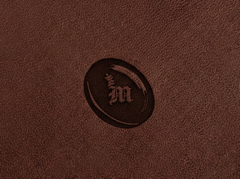 Dark brown leather surface with an embossed oval emblem featuring the letter M and a small floral design.