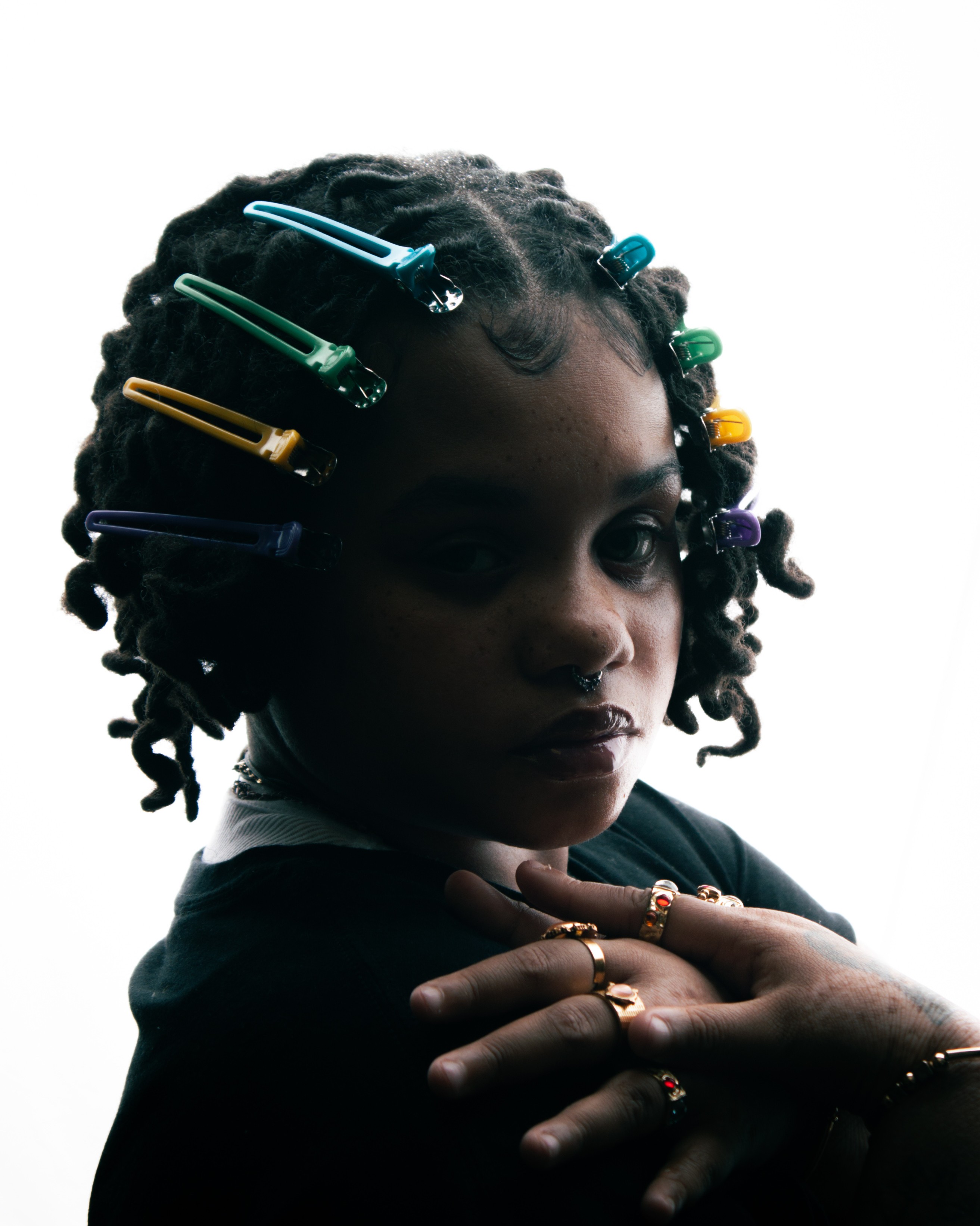 Person with colorful hair clips in curly hair and wearing multiple rings on crossed hands.