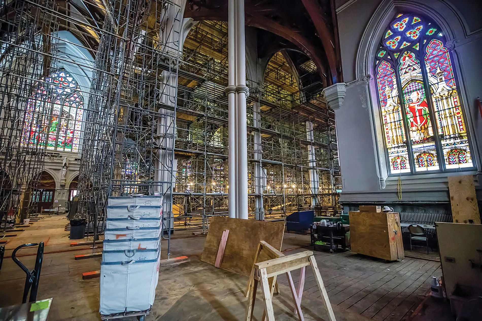 Intérieur d'une église avec rangées de bancs en bois, un pupitre central, et des fenêtres à volets sur les murs beiges.
