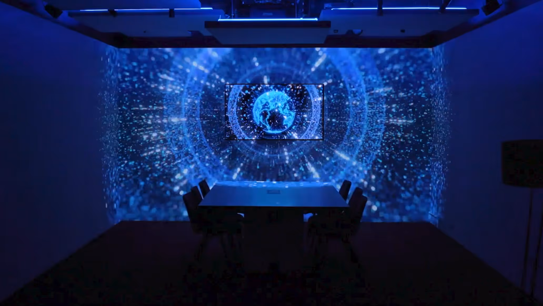 Dark conference room with blue digital globe and data visualization projected on walls around a table with chairs.