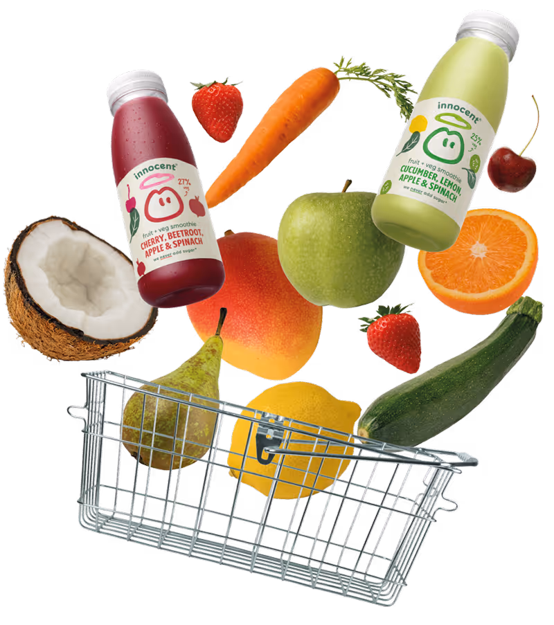 Two Innocent smoothie bottles with assorted fresh fruits and vegetables including coconut, strawberry, carrot, green apple, orange, cherry, pear, lemon, mango, and zucchini around a metal shopping basket.