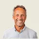 Smiling middle-aged man with gray hair and a light beard wearing a light gray collared shirt.