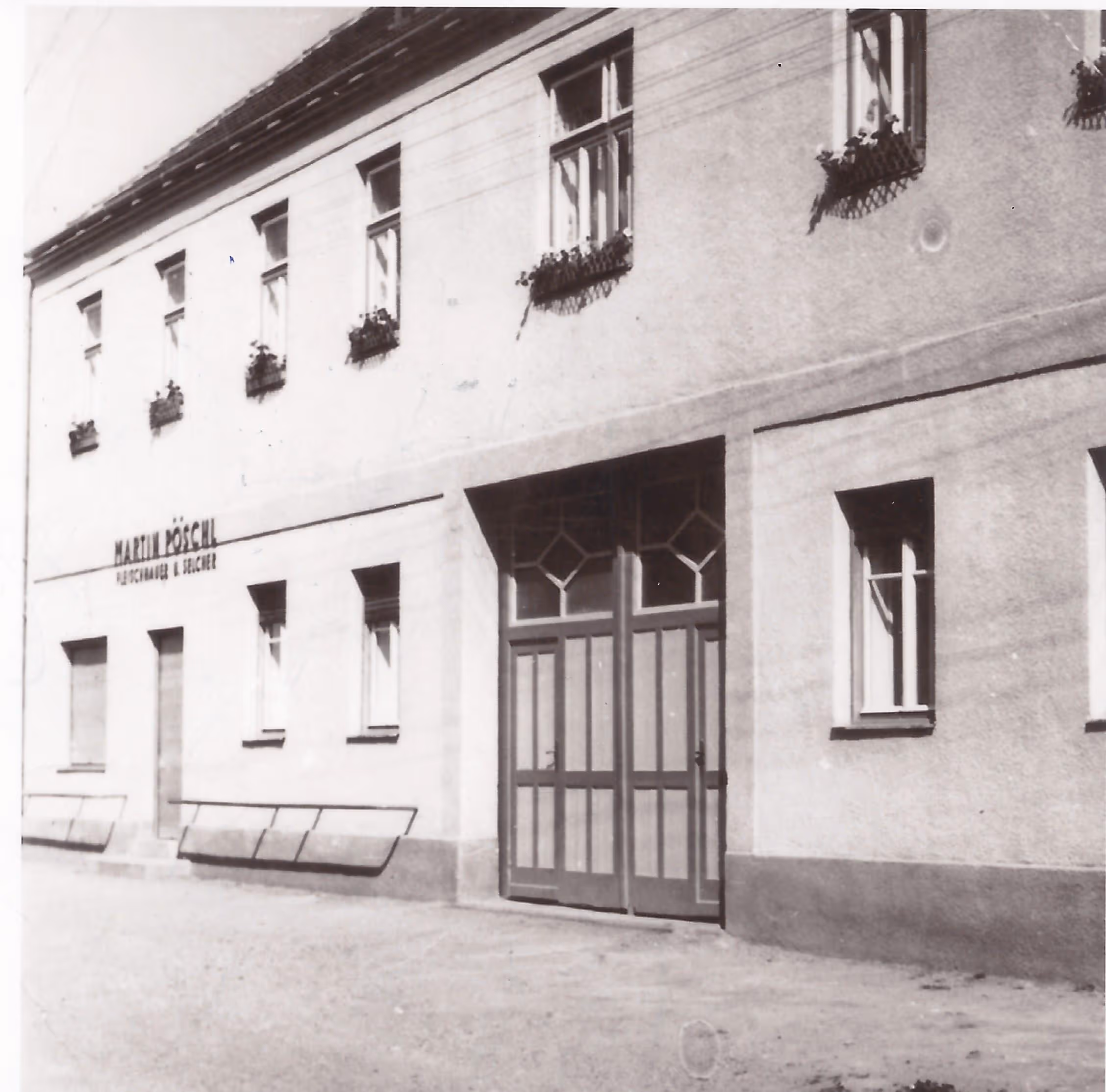 Black and white photo of a two-story building with multiple windows, flower boxes, and a large double door entrance.