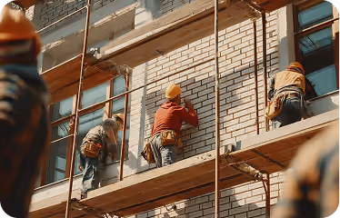 Construction workers wearing helmets and tool belts working on scaffolding against a brick building.