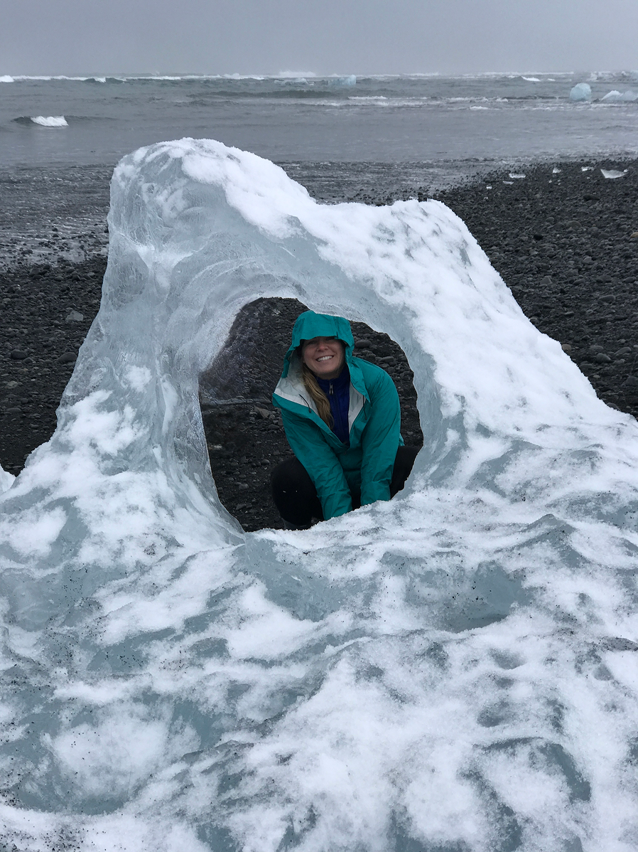 Girl looking though hole in iceberg on black sand beach in Iceland