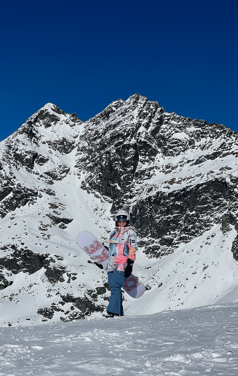 Girl in a snow suit holding a snowboard in the snowy mountains