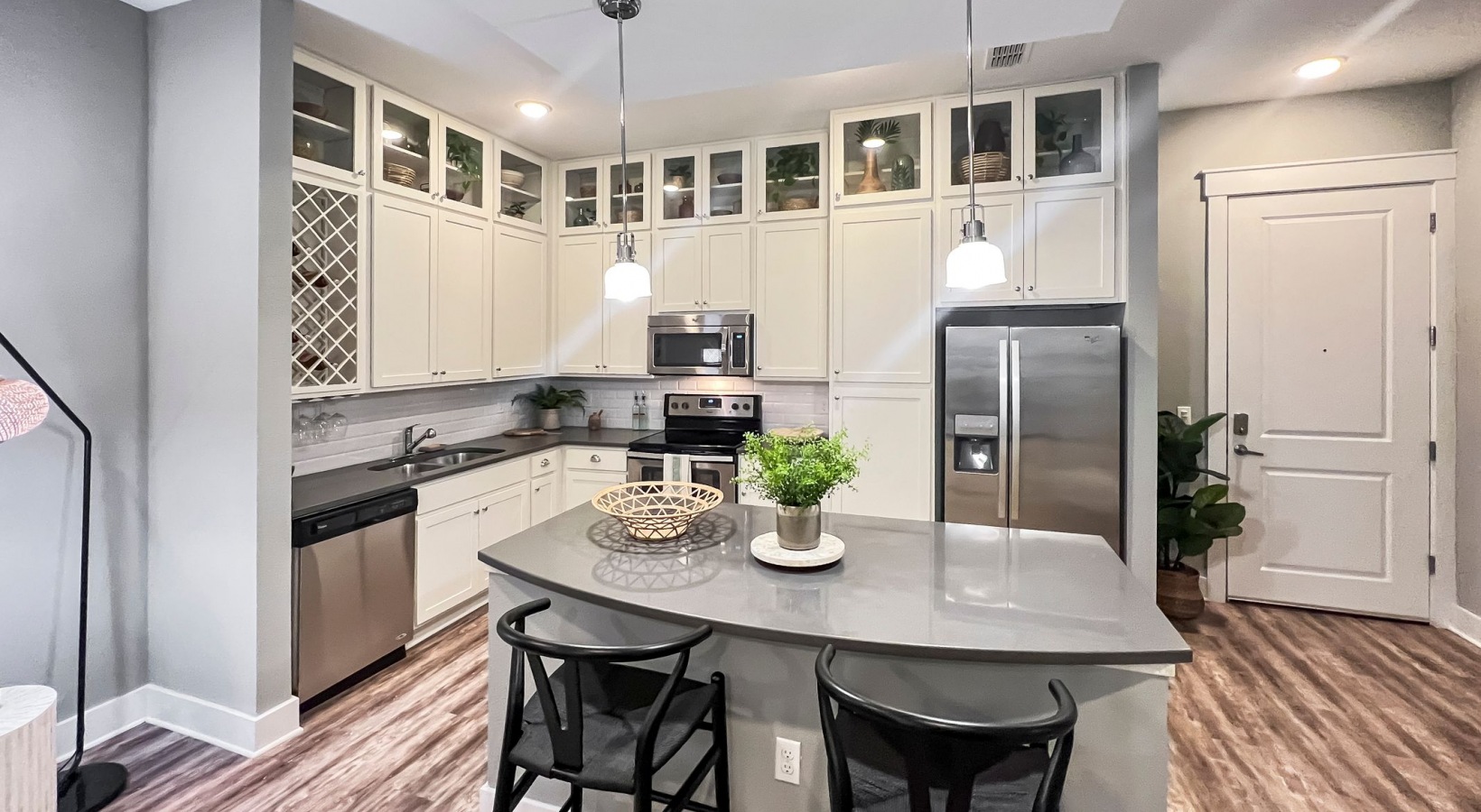 Spacious apartment kitchen with floating island, floor-to-ceiling cabinets, stainless steel appliances, and designer lighting