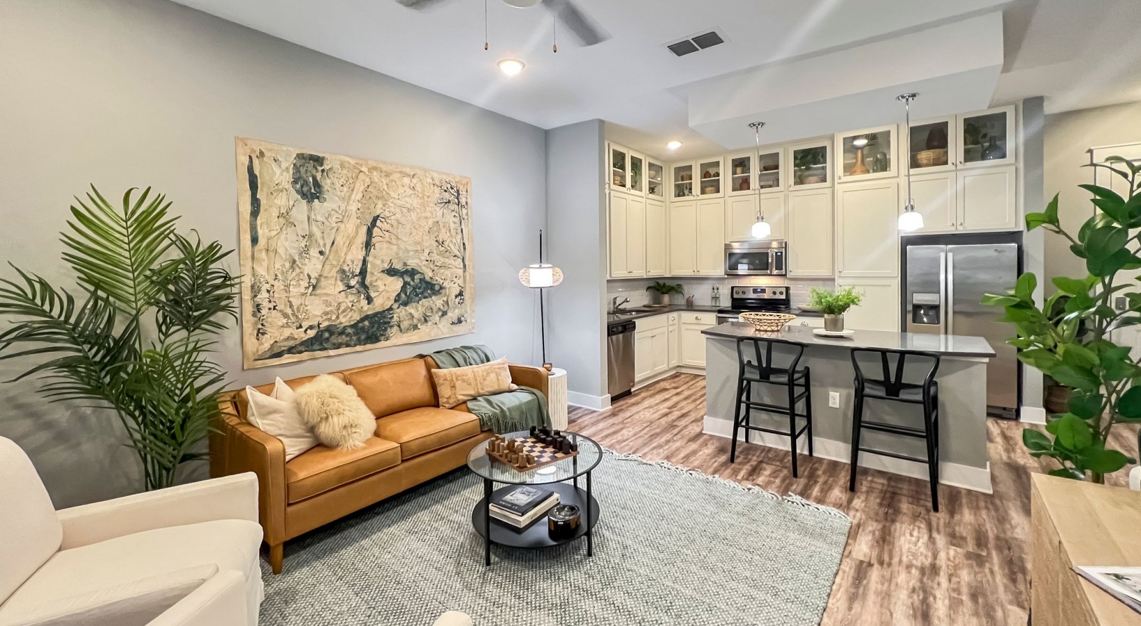 Apartment living area with couch, carpet, plants, and kitchen in background