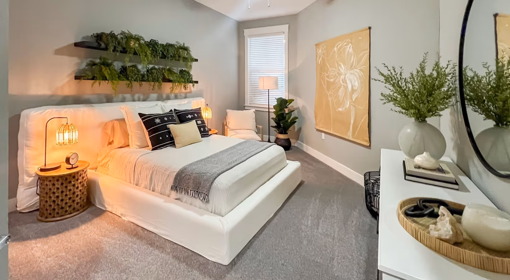 Furnished apartment bedroom with king sized bed, dresser, large window, and plants