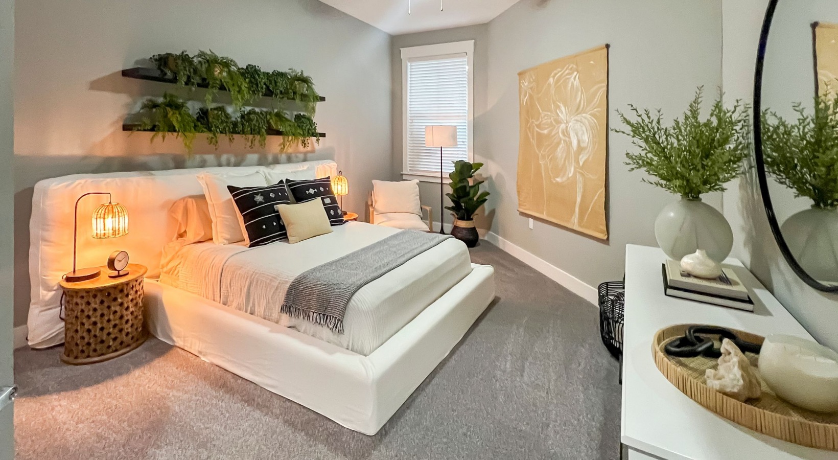 Furnished apartment bedroom with king sized bed, dresser, large window, and plants