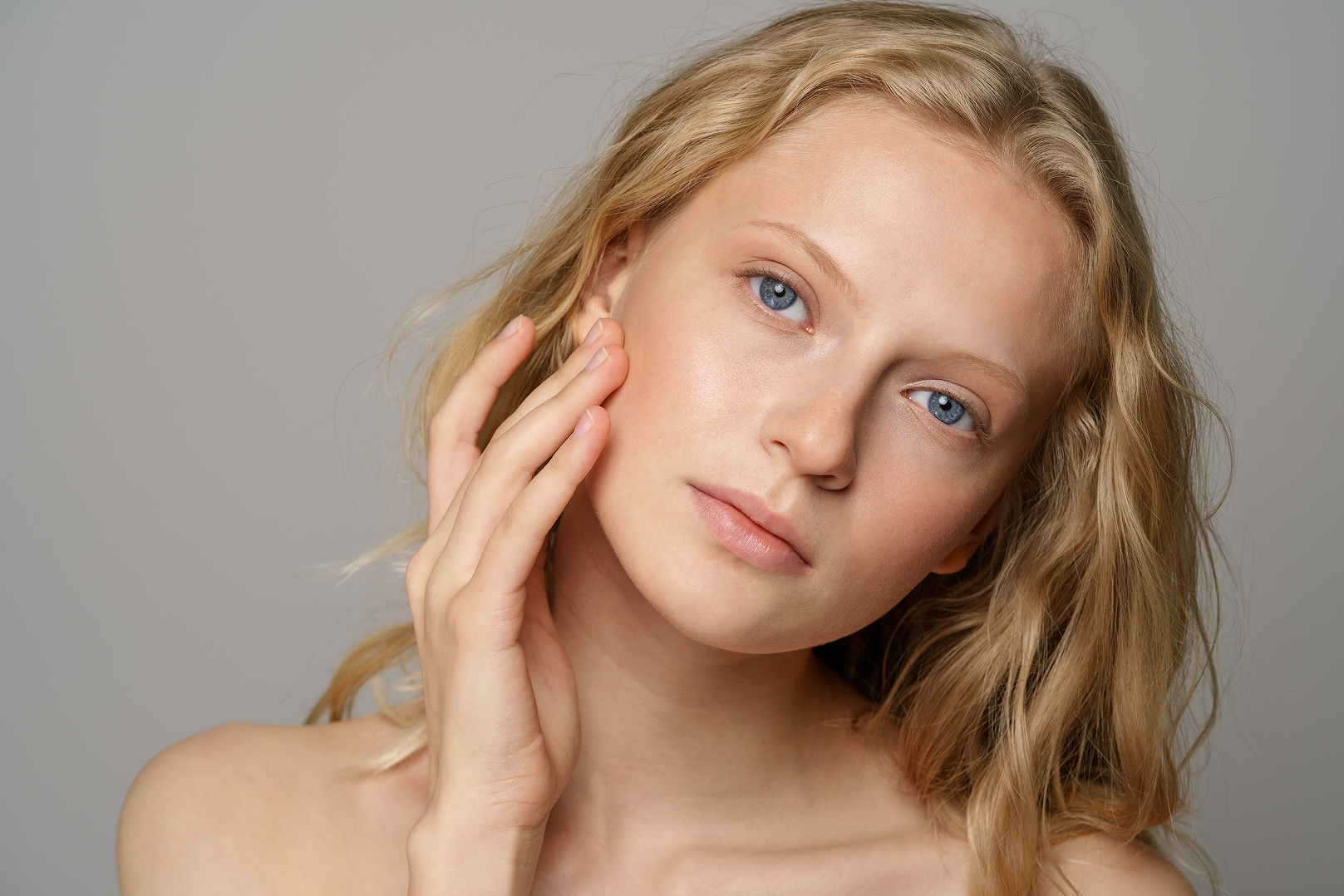 Close-up of a young woman with clear skin touching her cheek, looking calmly at the camera.
