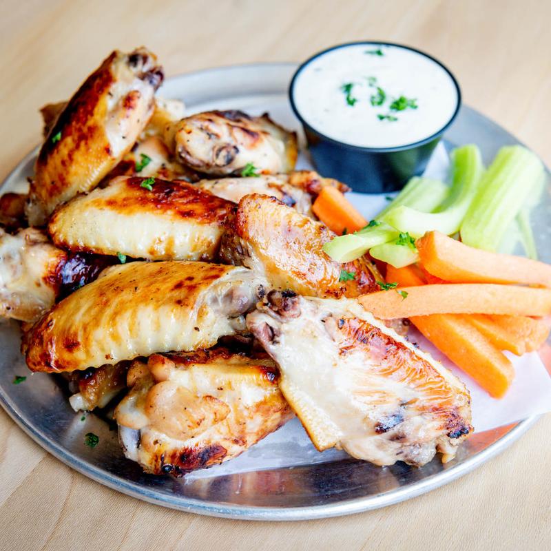 A plate of golden-brown chicken wings is served with a side of fresh carrot and celery sticks. A small cup of creamy dip accompanies the dish.