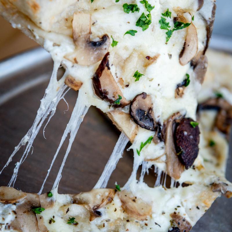 Close-up of a slice of mushroom pizza being lifted, with melted cheese stretching. Topped with fresh parsley, evoking a tempting, savory aroma.