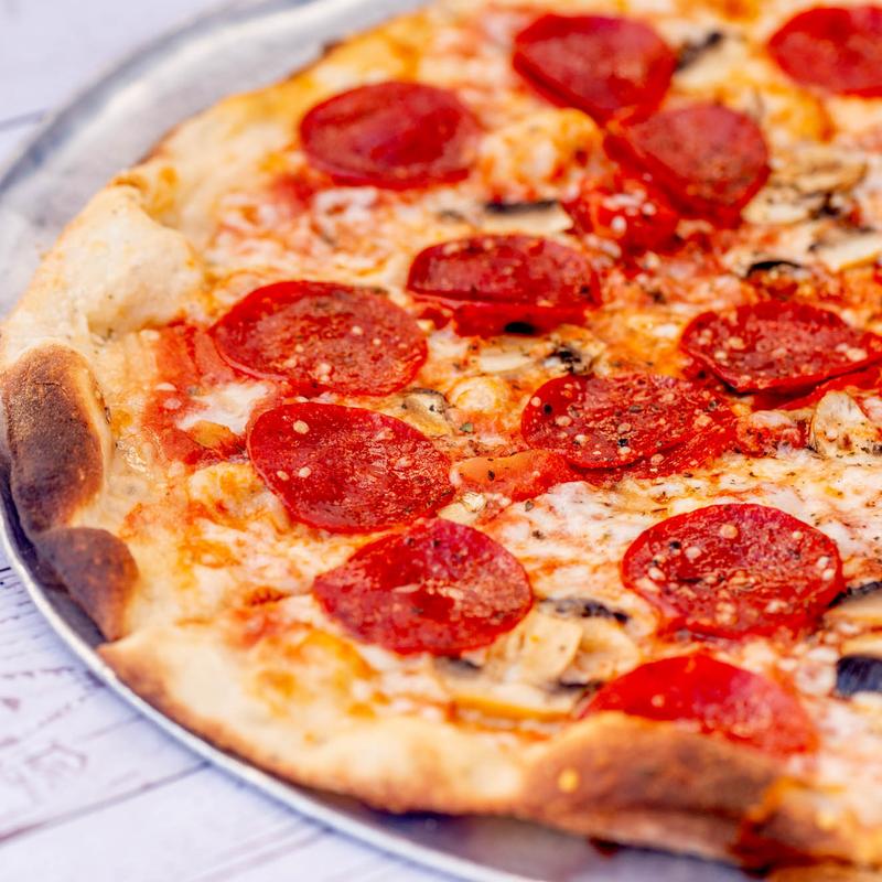 Close-up of a pepperoni pizza on a silver tray. The crust is slightly charred, with vibrant red pepperoni slices and melted cheese. Inviting and delicious.
