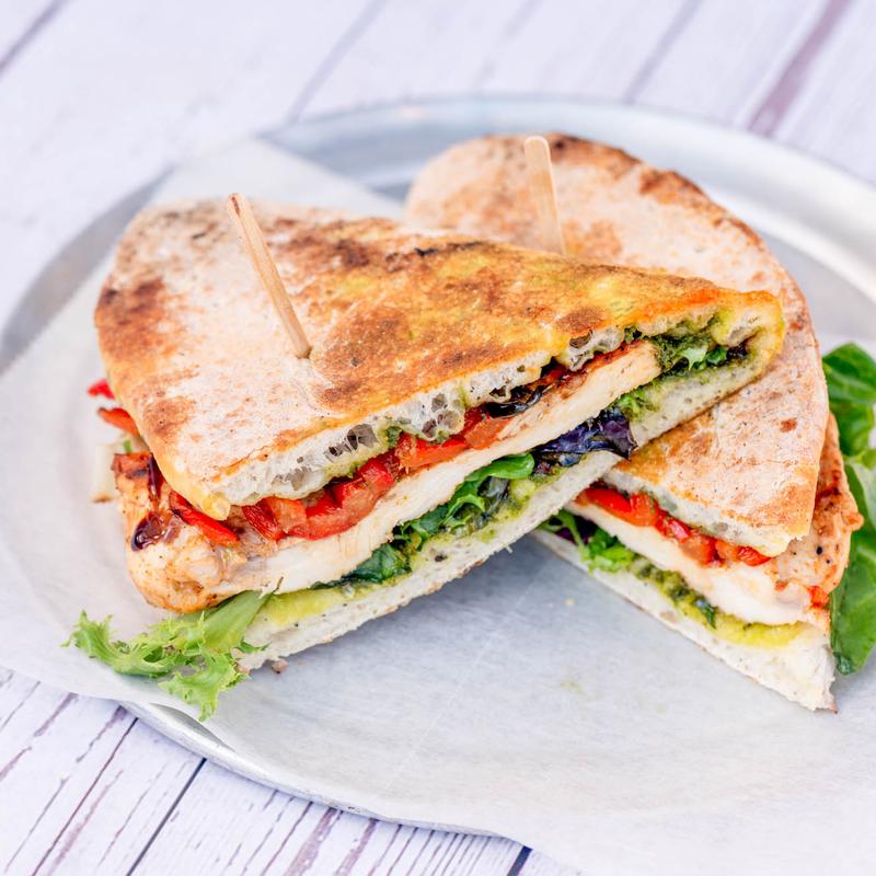 Grilled chicken panini with vibrant greens, red peppers, and melted cheese, served on a rustic plate. It evokes a fresh and appetizing feel.