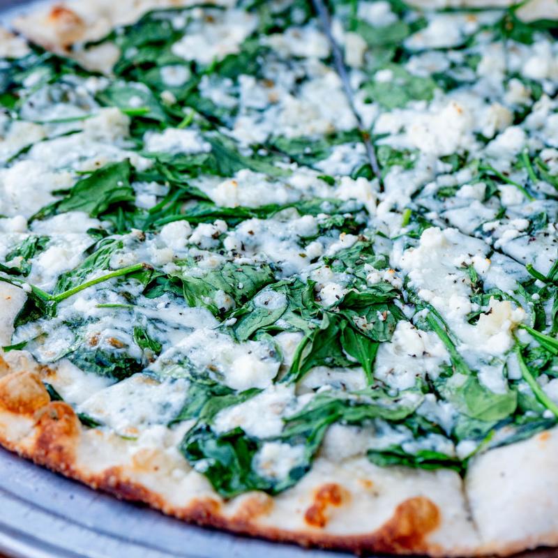 Close-up of a fresh spinach and feta pizza on a wooden board. The golden crust contrasts with the vibrant green spinach and creamy white cheese.