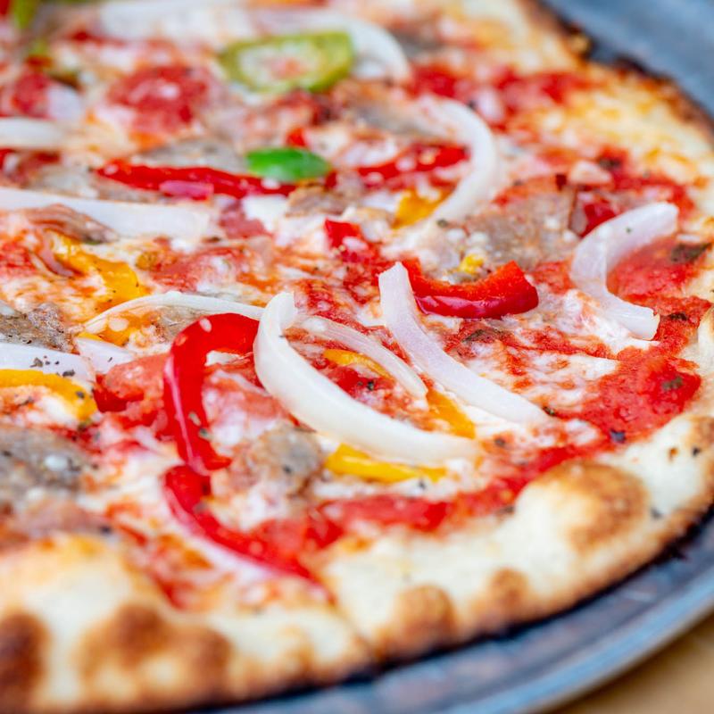 Close-up of a colorful pizza topped with red peppers, onions, sausage, and tomato sauce on a golden-brown crust, creating a fresh and appetizing look.