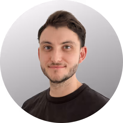 Porträt eines jungen Mannes mit dunklen Haaren, der ein schwarzes Shirt vor einem grauen Hintergrund trägt.