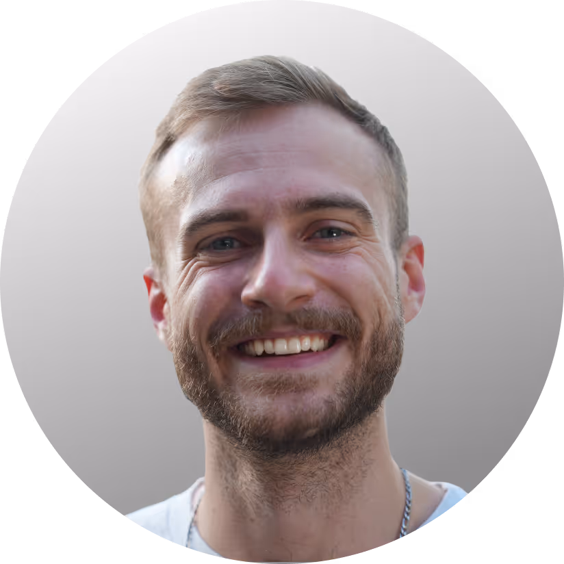 Lächelnder Mann mit heller Haut, kurzem blondem Haar und Bart vor neutralem Hintergrund.