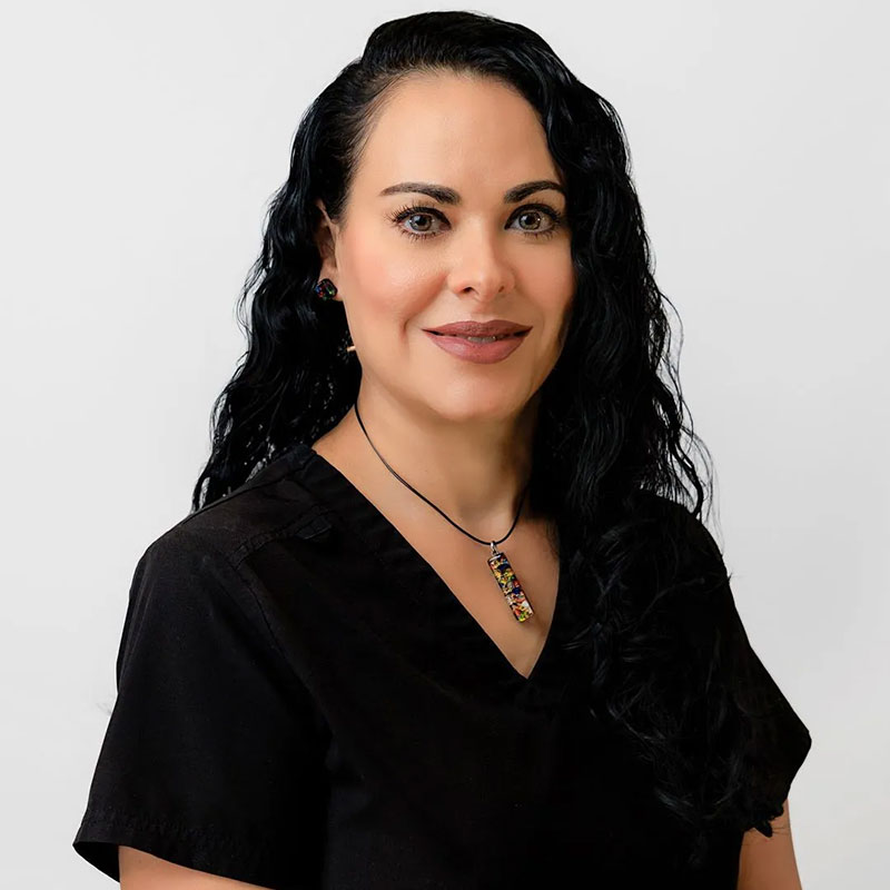 Woman with long black hair wearing a black top and necklace, smiling against a plain background.