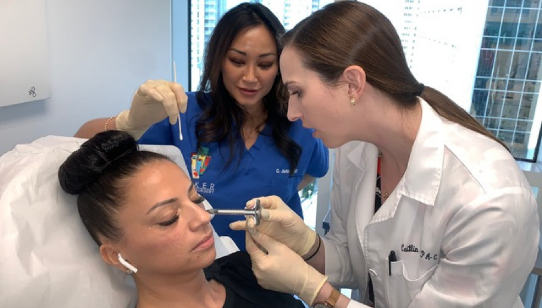 Medical professional in white coat administers facial injection while assistant holds cotton swab by patient's face.