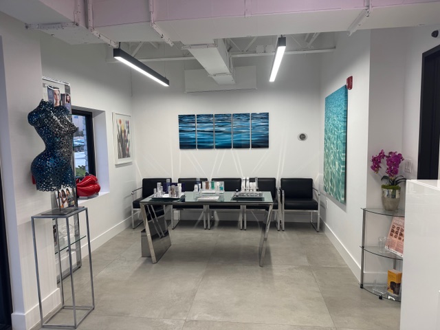 Modern waiting area with glass table, black chairs, colorful wall art, and a decorative mannequin stand.
