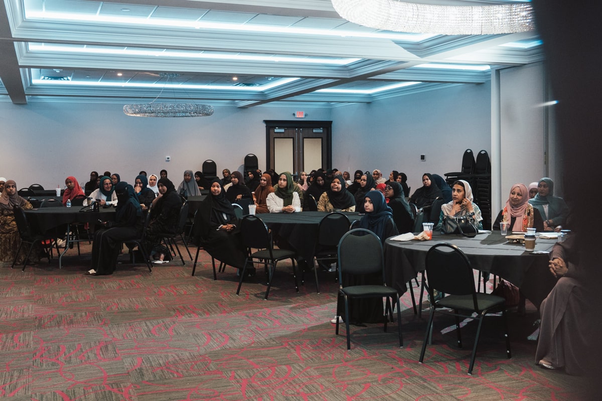Two people tend to a vertical garden of black triangular pots with various green plants against a green and white grid, evoking a sense of urban gardening.