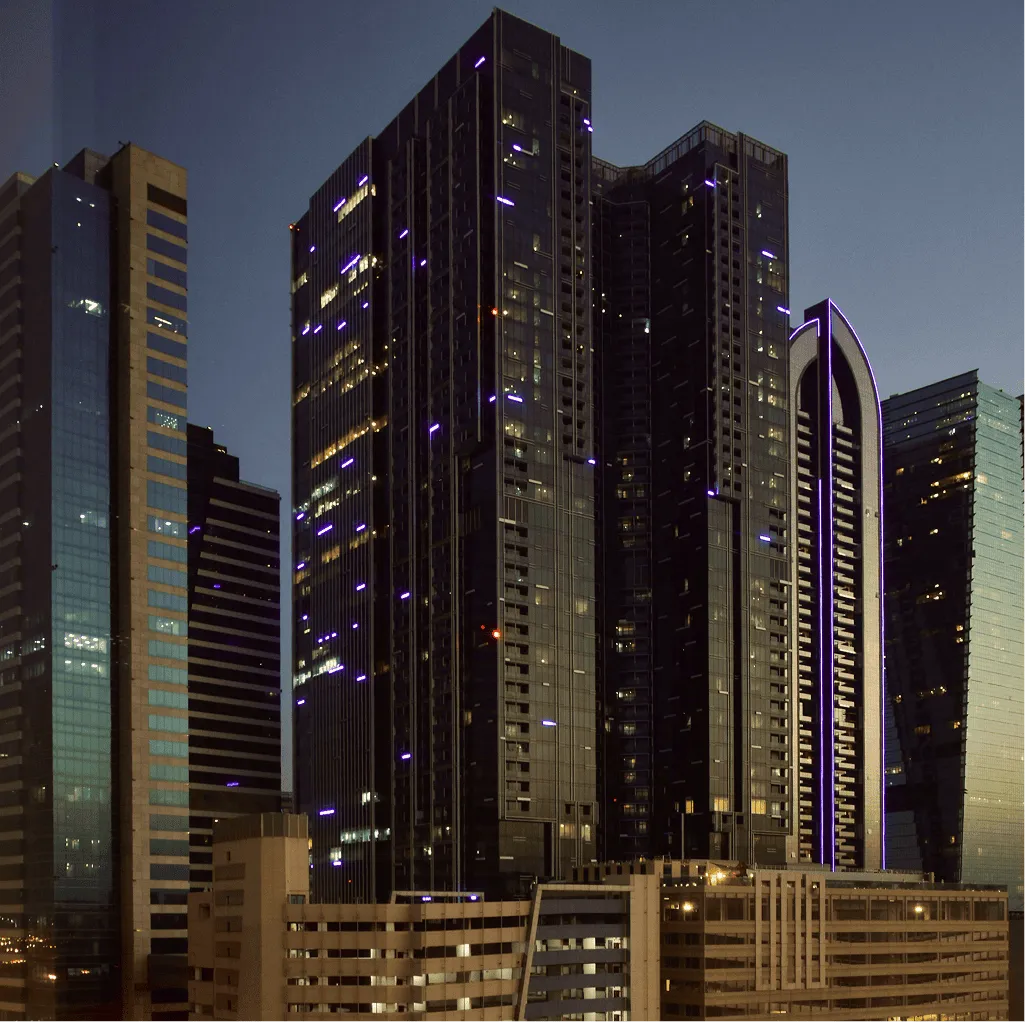 Cluster of modern high-rise buildings at dusk with illuminated windows and purple accent lights.