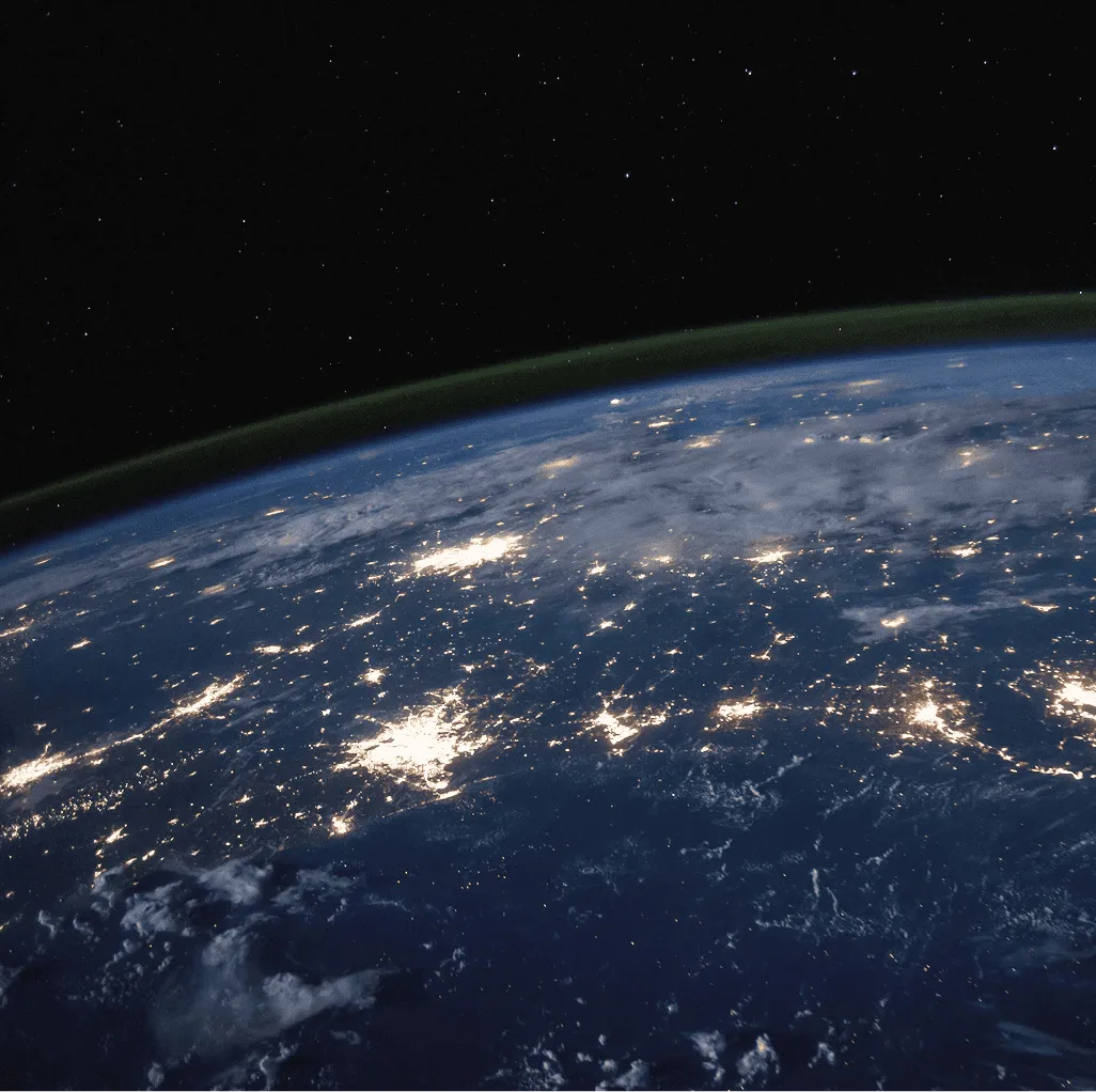 Night view of Earth from space showing illuminated city lights and a starry sky.