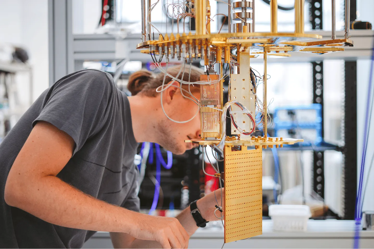 Scientist inspecting a complex quantum computing device with gold and transparent components in a lab.