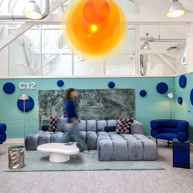 Modern lounge area with blue and gray upholstered modular sofa, blue accent chairs, round white coffee table, and large layered orange pendant light.